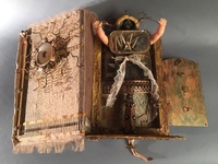 <div class='title'>Mama Mia</div><br>Vintage encyclopedia, found objects of metal wood, fabric, doll parts, photo of artist's painting on canvas, copper-backed glass tiles, mirror, vintage pins and fabric, vintage letter, soil <br>Closed: 8"w x 8"h x 14"d; Open: 6"w x 18.5"h x 14"d<br>